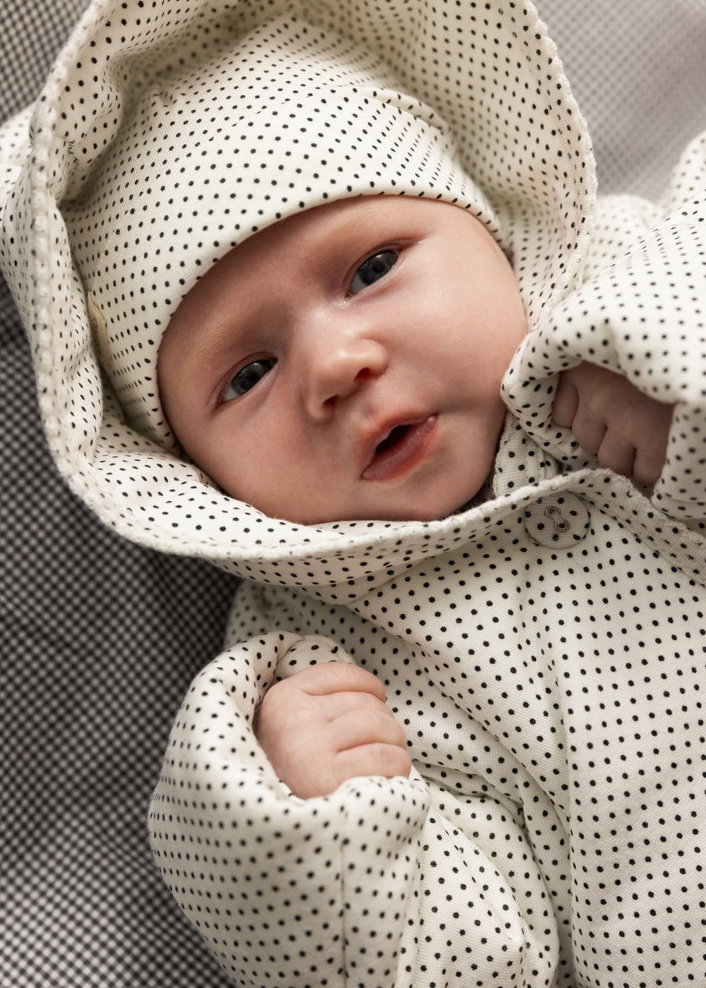 Baby i hvid hættet jakke med små sorte prikker og knaplukning