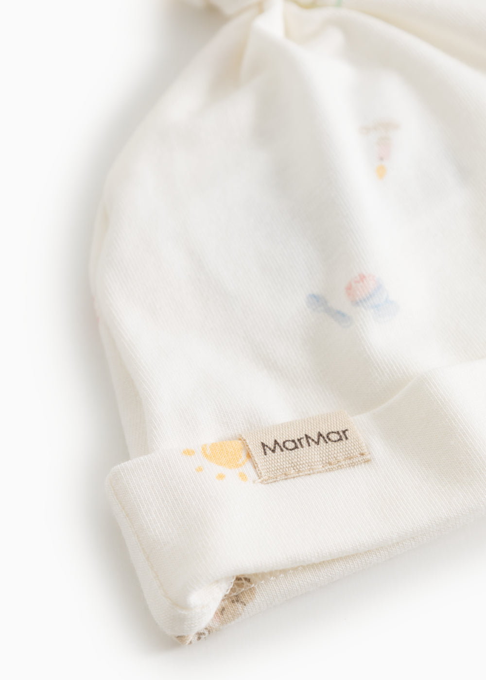 Hvid babyhue med knude og elastisk kant samt MatMar-mærke på bånd.