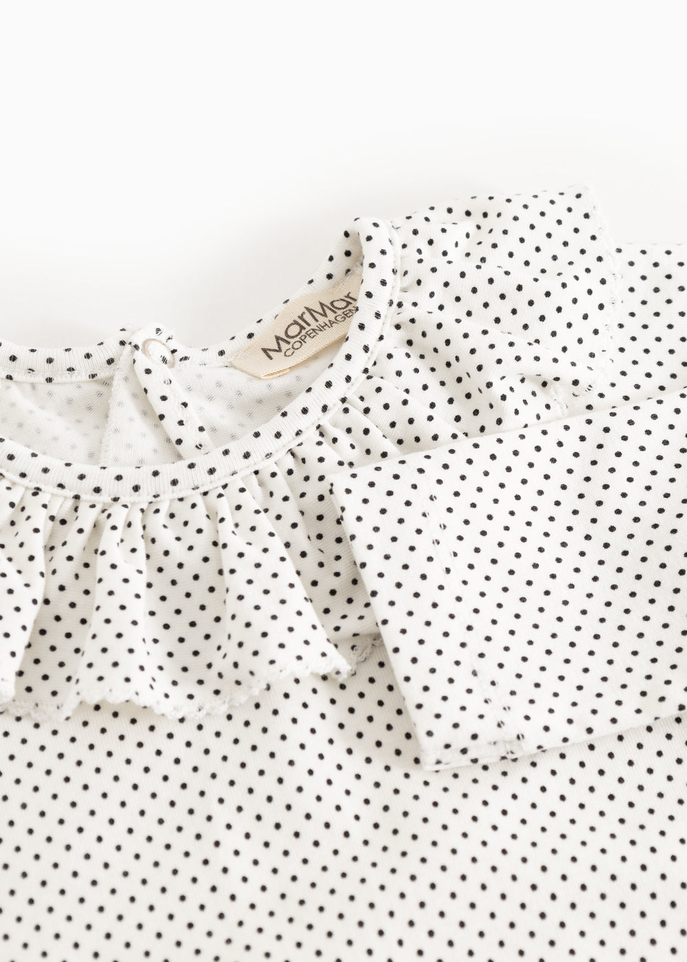 Detalje af baby-bodystocking med små sorte prikker og flæsekant ved halsudskæring