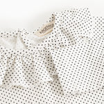 Detalje af baby-bodystocking med små sorte prikker og flæsekant ved halsudskæring