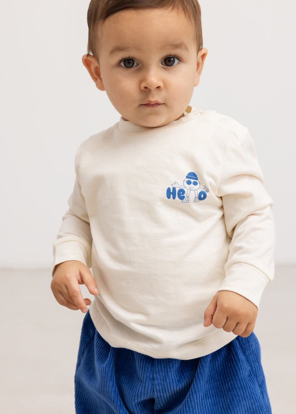 Langærmet bluse i creme med blåt “Hello” print på brystet.
