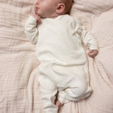 Hvid babyheldragt med knaplukning foran, båret af sovende spædbarn