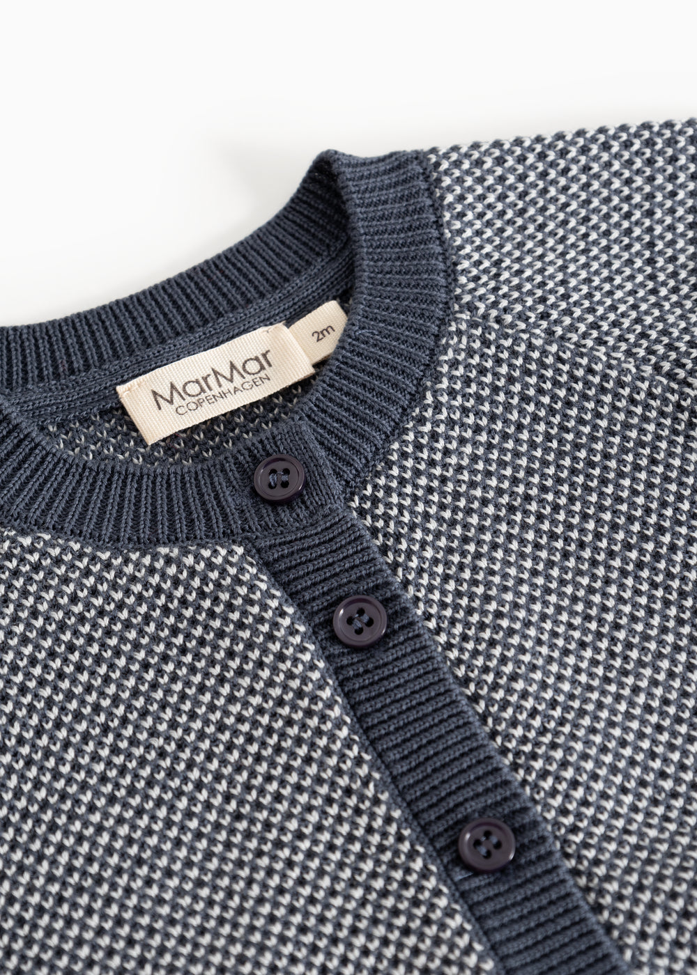Detalje af strikket cardigan med knaplukning og rund halsudskæring i rib