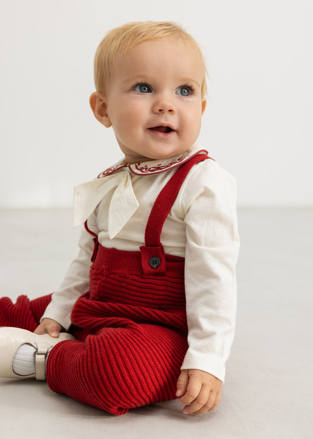 Røde strikbukser med seler til baby, set mens barnet sidder