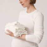 Gravid kvinde iført hvid t-shirt og holder foldet babytøj