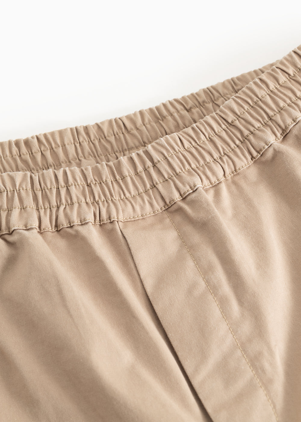 Detalje: beige bukser med elastisk linning og syninger ved taljen.