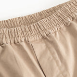 Detalje: beige bukser med elastisk linning og syninger ved taljen.