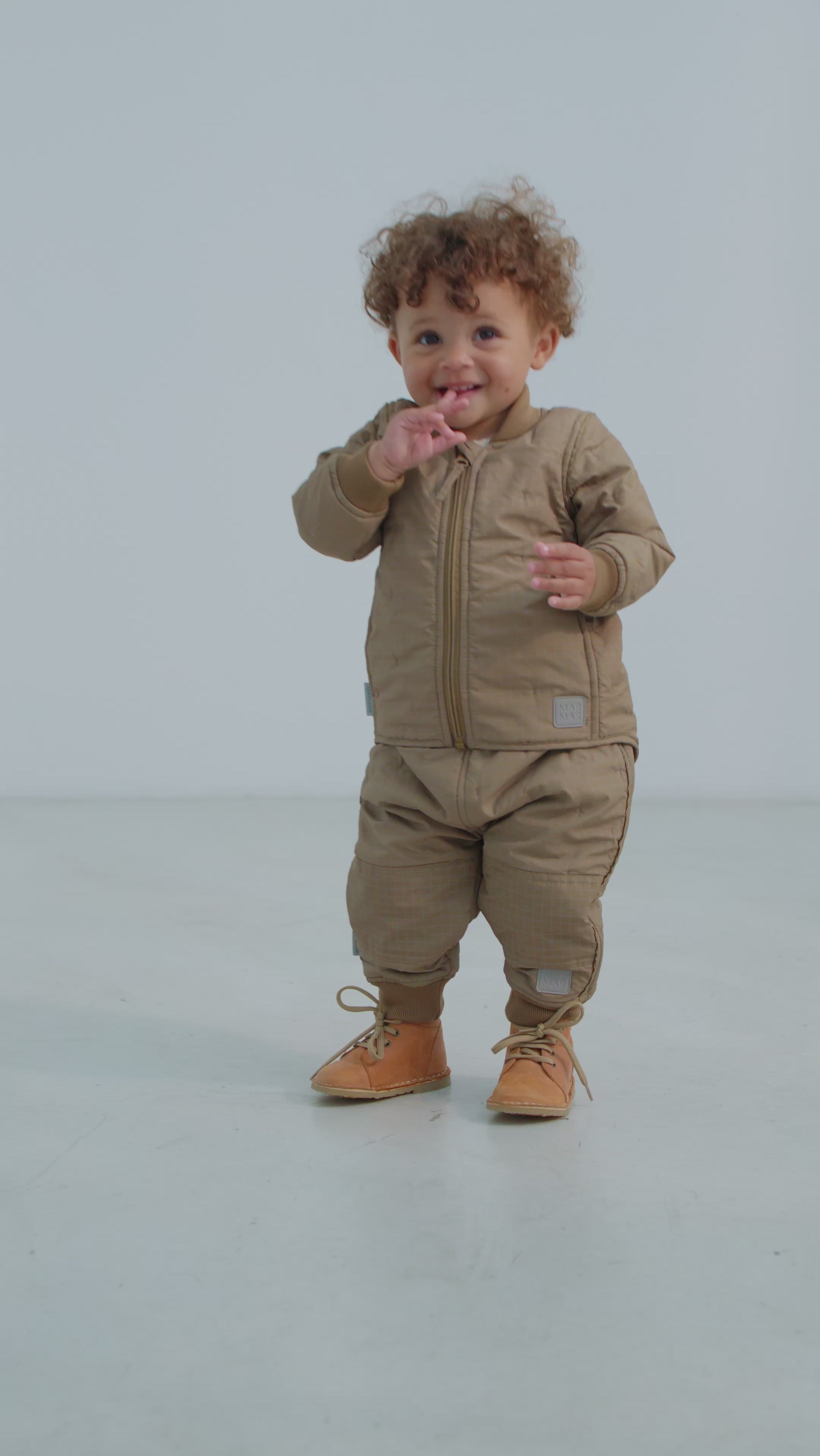 Baby iført beige termotøj - jakke med lynlås, termobukser  og støvler