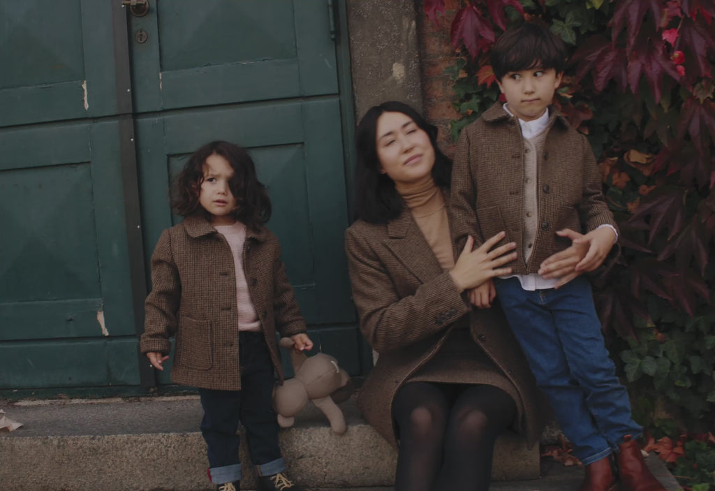 Mor og børn iført brune blazere foran grøn dør