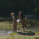 To børn leger udendørs ved vand i beige regntøj