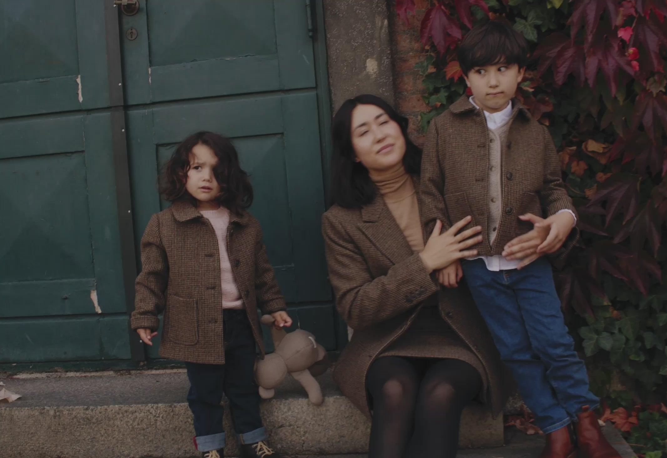 Mor og børn iført brune jakker foran grøn dør