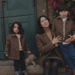 Mor og børn iført brune uldfrakker foran grøn dør