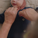 Baby får hjælp til at tage beige uldhue på