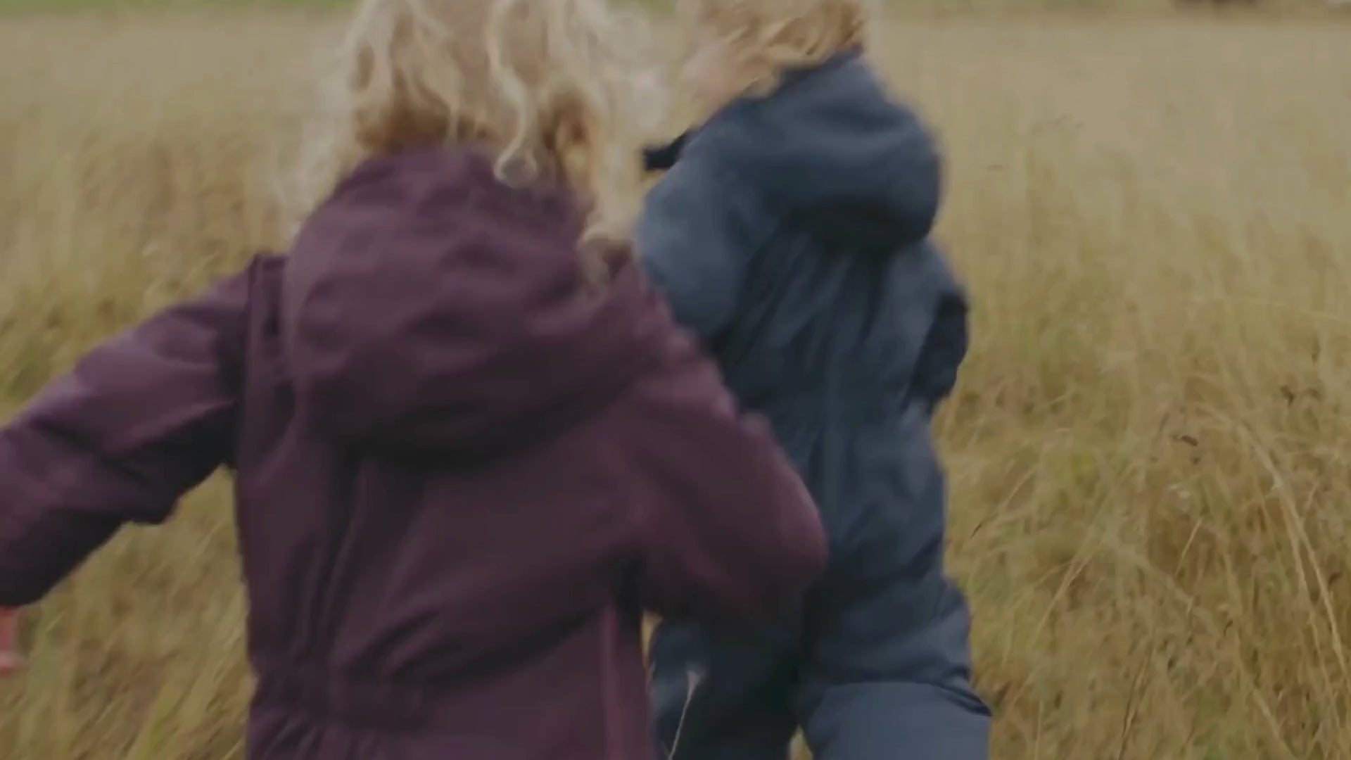 To børn iført termoheldragter leger og løber i græsset