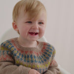 Smilende baby iført beige uldstrikbluse med mønster