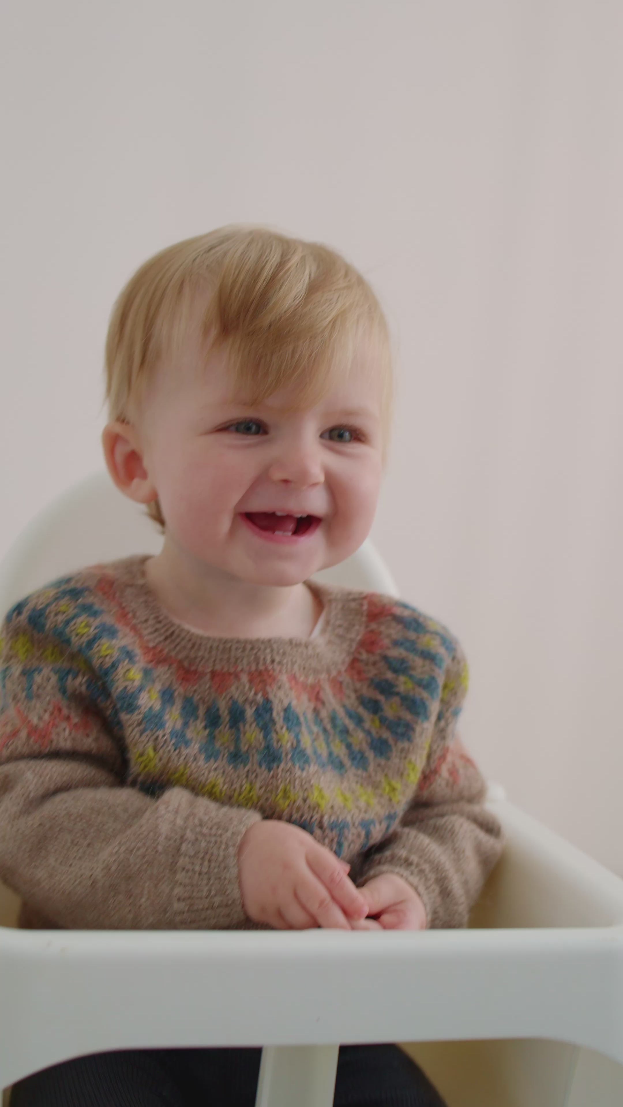 Smilende baby iført beige uldstrikbluse med mønster