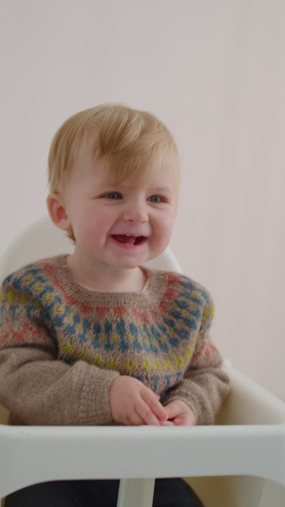 Smilende baby iført beige uldstrikbluse med mønster